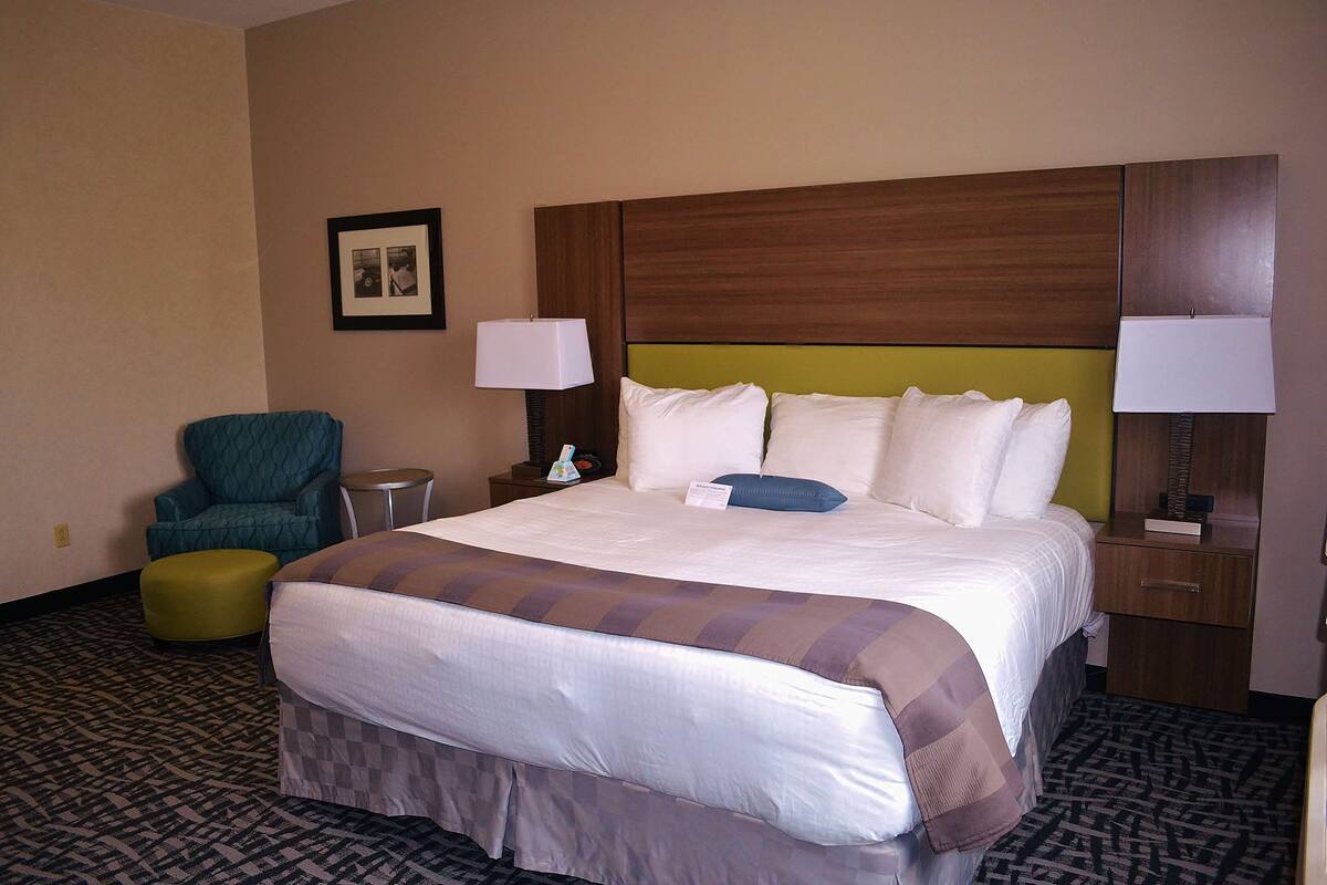 A hotel room with a large bed, two bedside lamps, a green chair, and a small table.