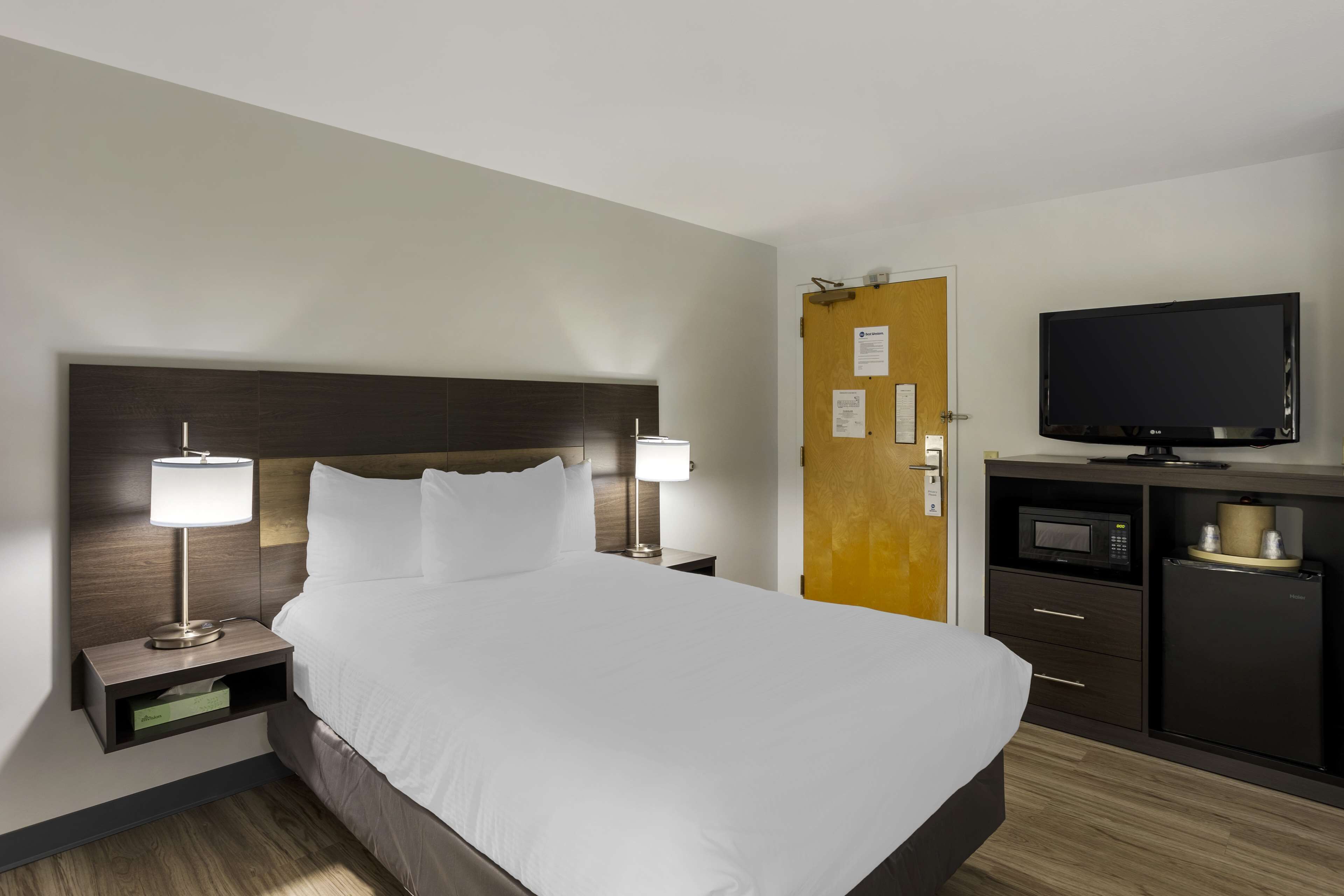 Ein Hotelzimmer mit einem großen Bett, Nachttischlampen, einem Fernseher, einer Mikrowelle und einer Minibar.