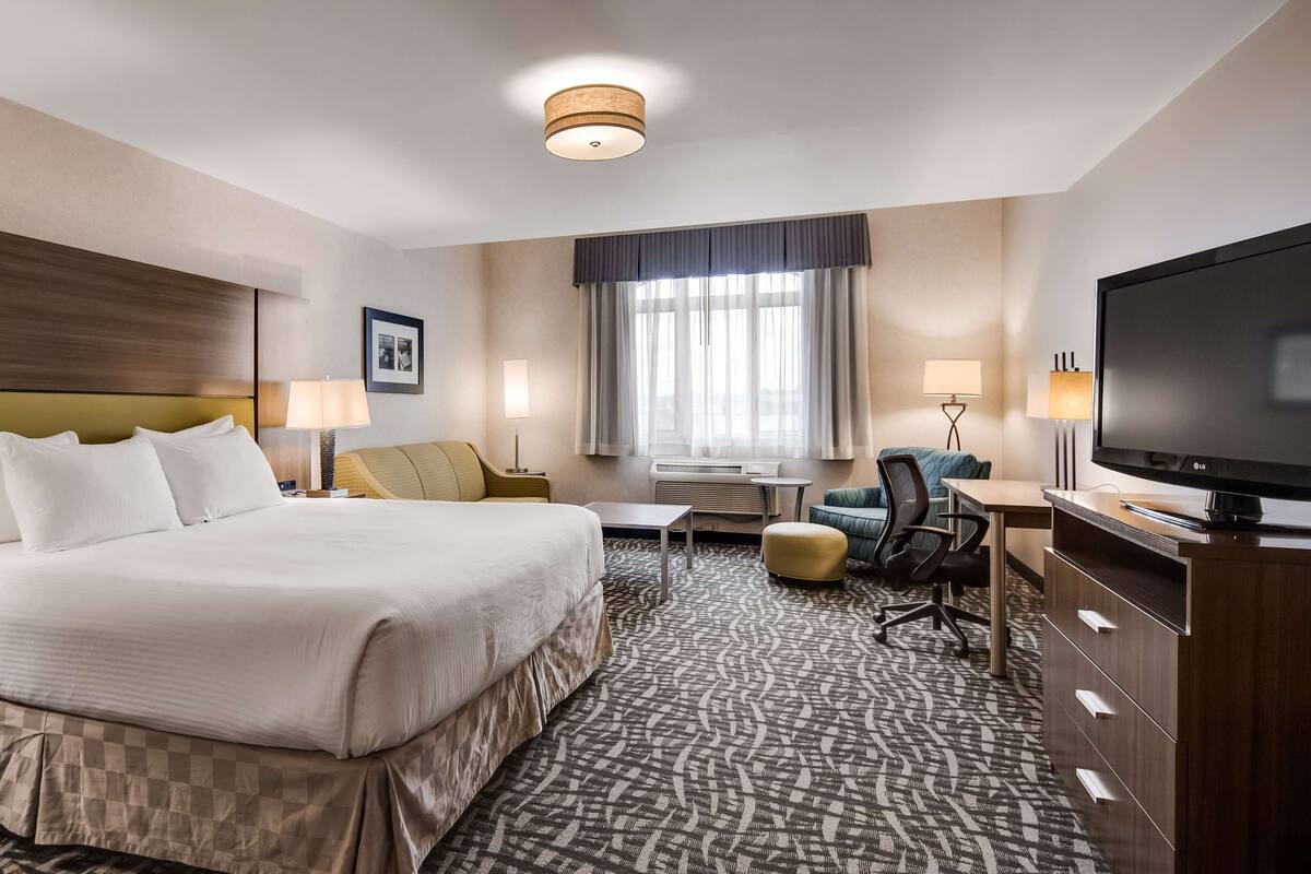 A hotel room with a large bed, a desk, a television, and a seating area.