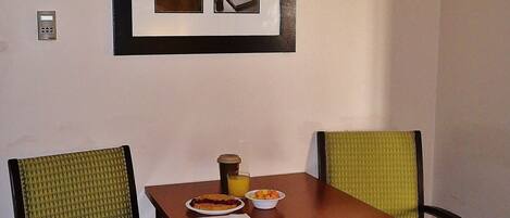 Un pequeño comedor con una mesa y dos sillas, un cuadro enmarcado sobre la mesa y un interruptor de luz en la pared.
