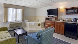 A compact hotel room with a kitchenette, a flat-screen TV, a large window with curtains, a bathtub, and a seating area with a sofa and a small table. - Best Western DuBois Hotel (DuBois)