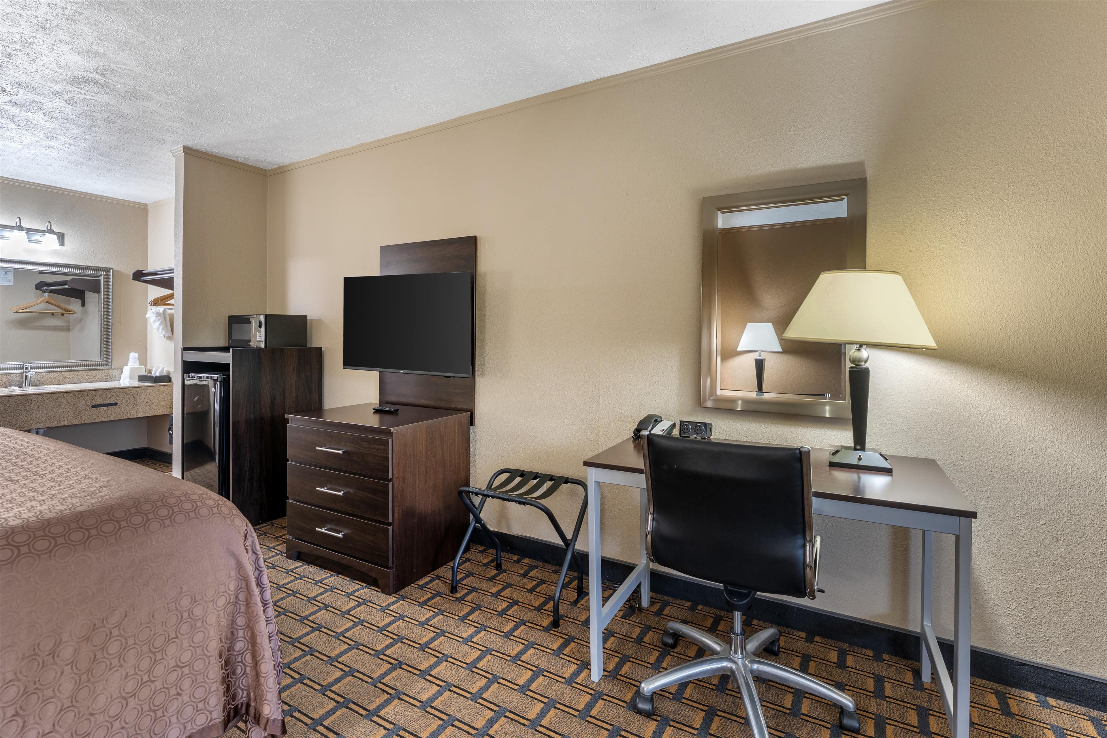 Una habitació d'hotel amb un llit, escriptori, cadira, televisió, làmpada i mirall.