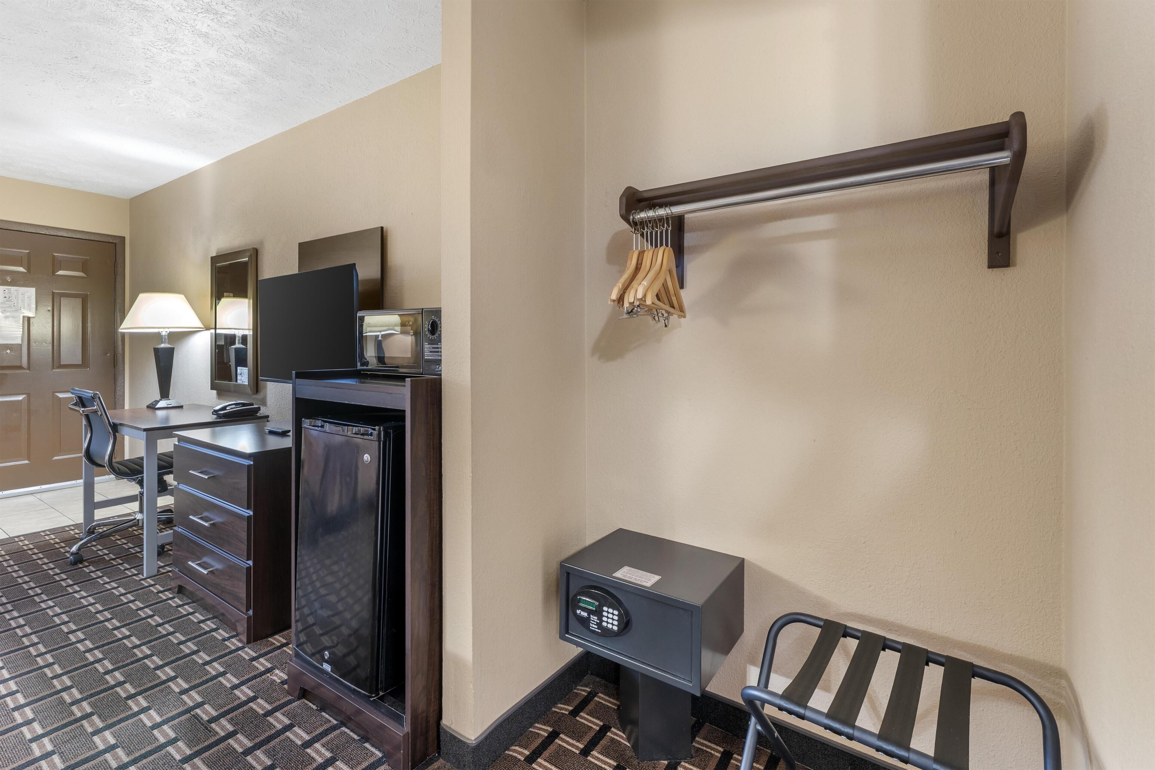 A hotel room with a desk, chair, minibar, television, and a safe.