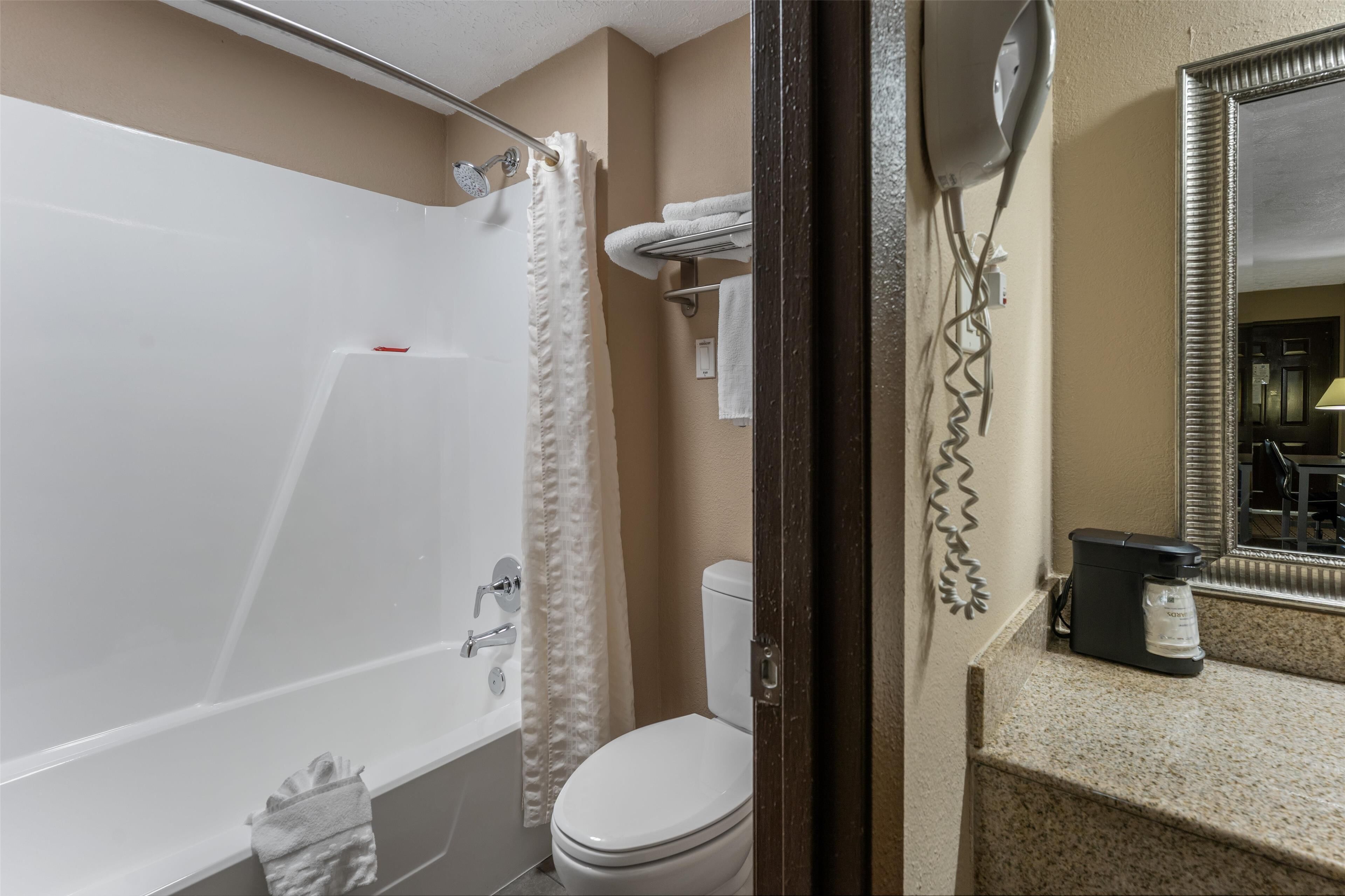 A bathroom with a bathtub, toilet, and a coffee maker on the counter.