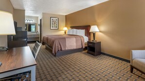 A hotel room with a bed, bedside table, lamp, and a desk with a chair.