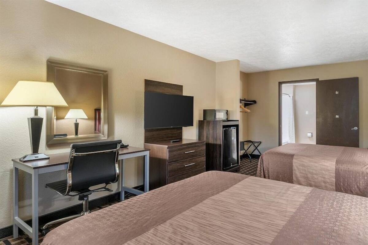 Habitación de hotel con dos camas, un escritorio con silla, televisor, refrigerador y una puerta.