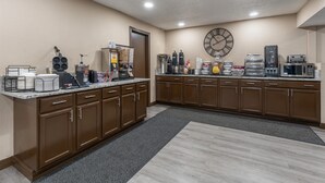 A kitchen with brown cabinets, a clock, and various appliances like a coffee maker and microwave.