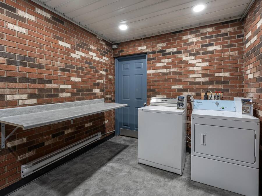 A laundry room with brick walls, a blue door, and two washing machines.