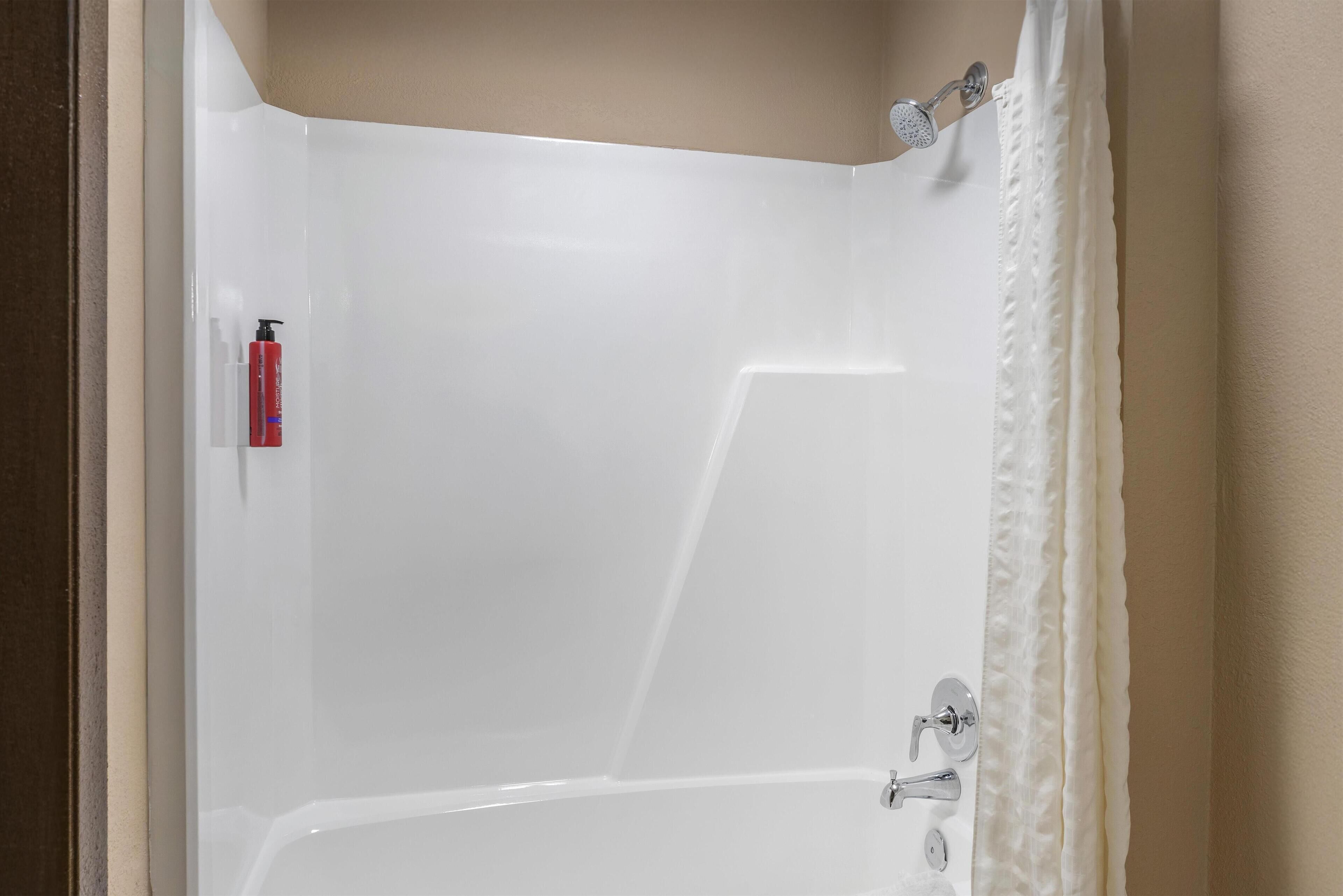 A white bathtub with a showerhead and a red bottle on the left.