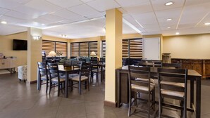 A spacious dining area with multiple tables and chairs, a television mounted on the wall, and a window with blinds. - SureStay Hotel by Best Western St. Pete Clearwater Airport (Clearwater)