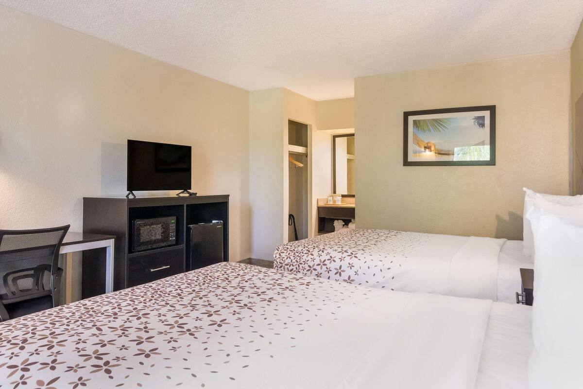 Una habitación de hotel con dos camas, un escritorio con televisor, un microondas y un armario.