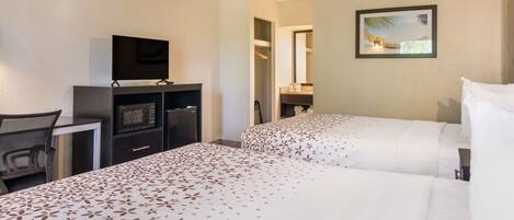 A hotel room with two beds, a desk with a TV, a microwave, and a closet.