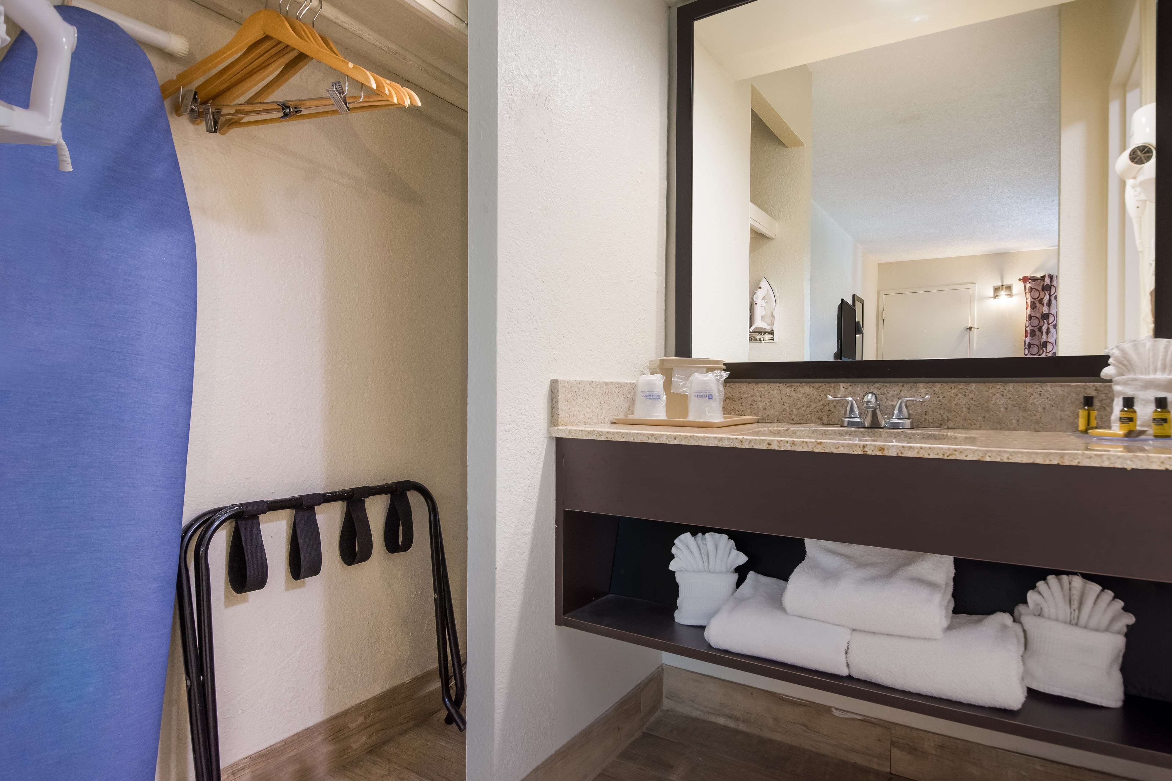Un baño con lavamanos, espejo, toallero y repisa con toallas dobladas.