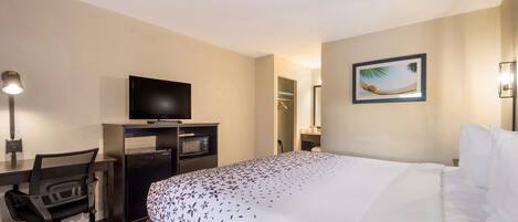 Una habitación de hotel con una cama, un escritorio con ordenador y televisor, una silla y un armario.