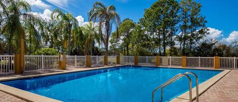 Una piscina rectangular con una escalera metálica en un lateral, rodeada por una valla blanca y árboles.