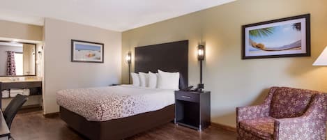 Habitación de hotel con cama, una silla, escritorio, mesita de noche y lámpara de pared.