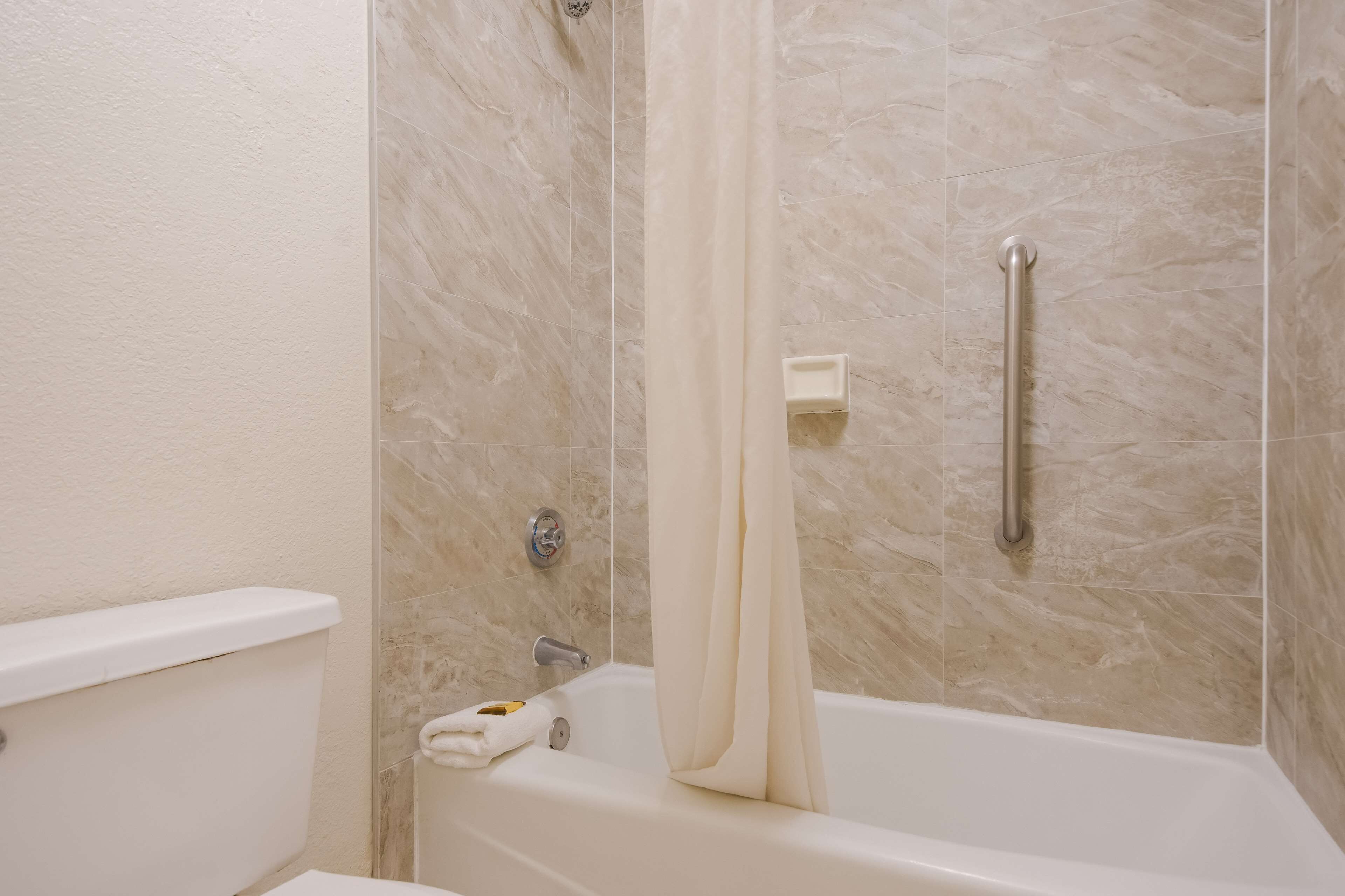 A bathroom with a bathtub, a shower curtain, a handrail, and a soap dish.
