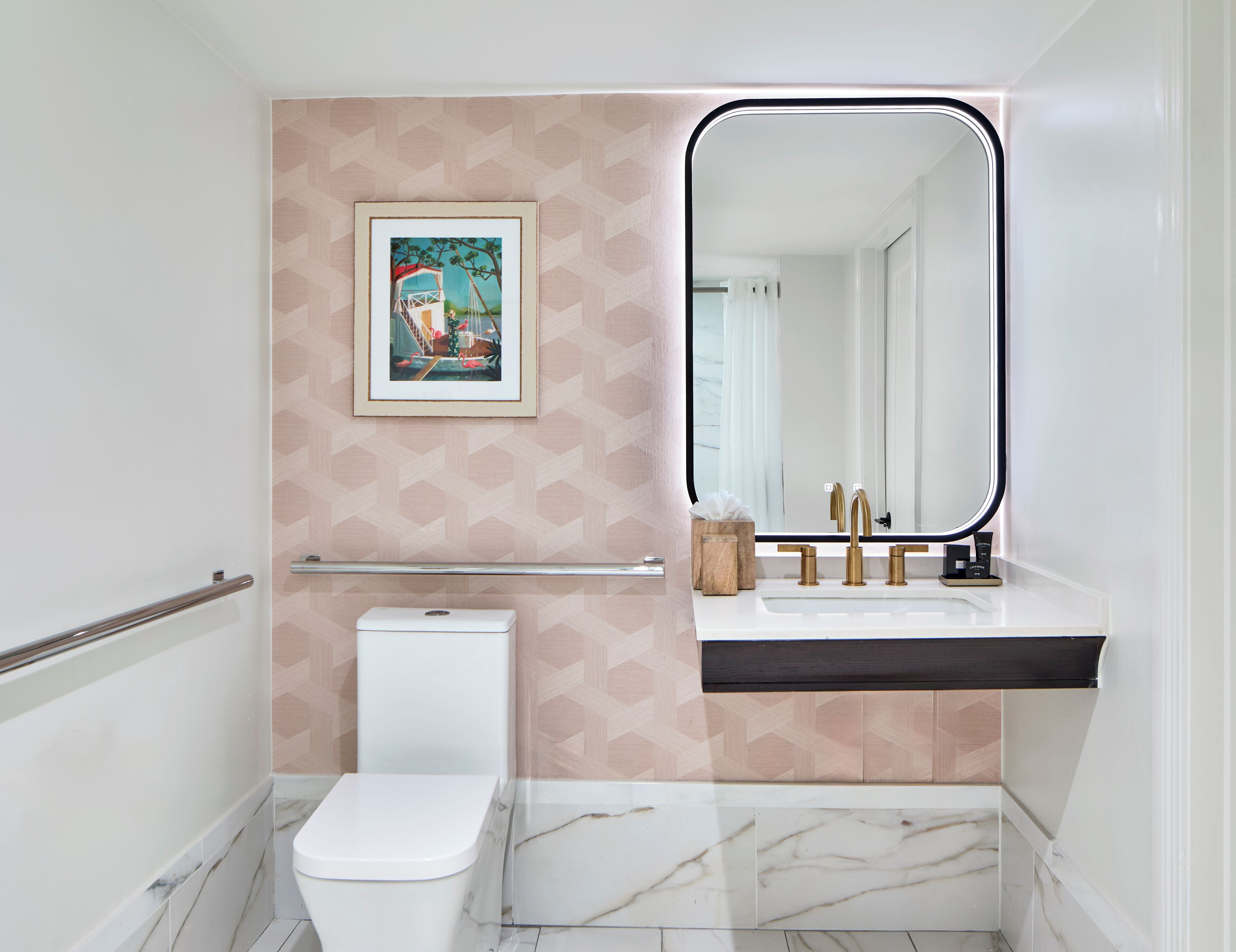 A modern bathroom with a toilet, a sink with a mirror, and a framed picture on the wall.