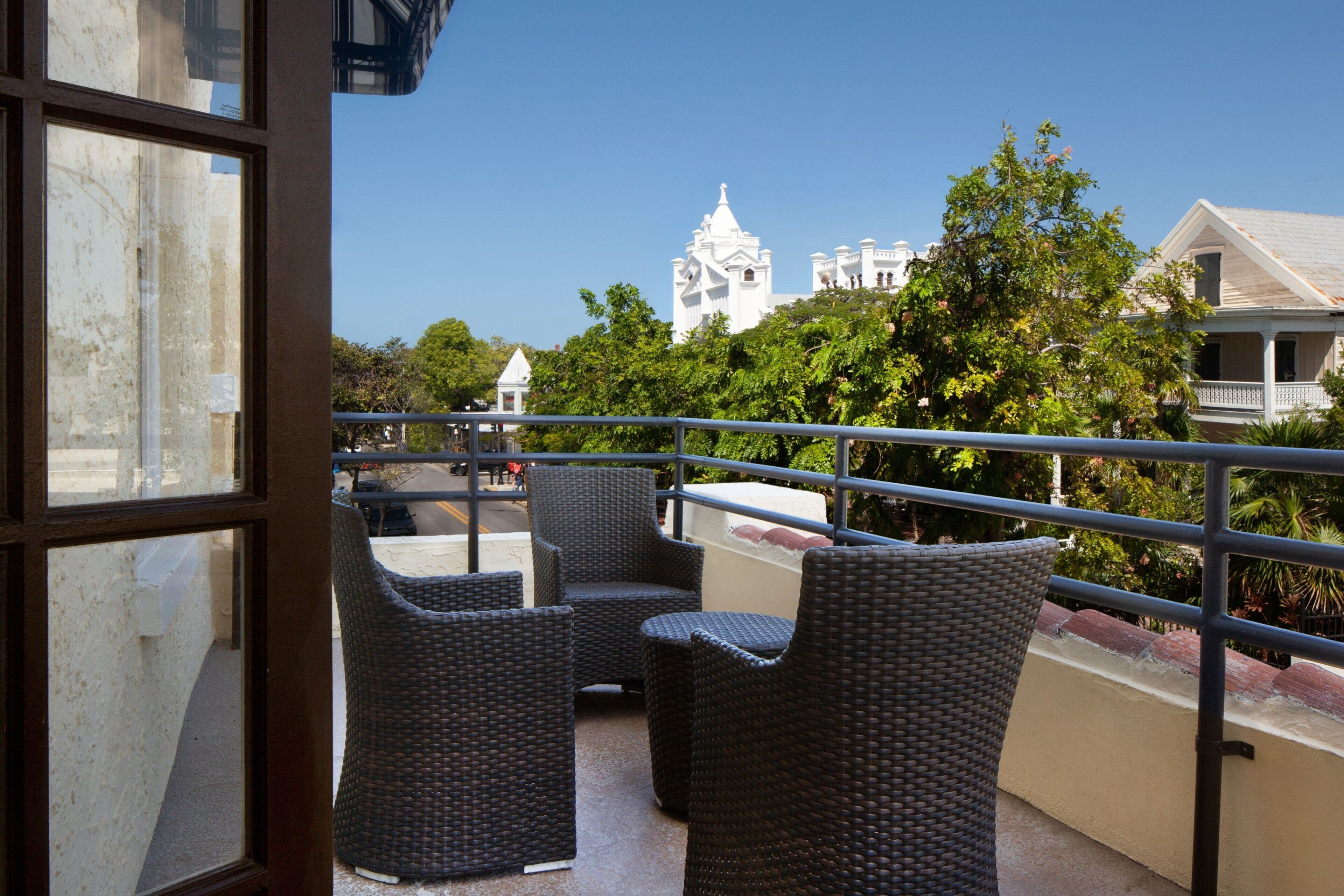 A balcony with wicker furniture, a railing, and a view of a white building with a tower.