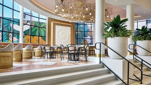 A spacious lobby with a checkered floor, a central seating area with wicker chairs, a large potted plant, and a staircase with a metal railing. - La Concha Key West, Autograph Collection (Key West)