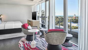 A modern hotel room with a large window, a bed, a TV, and a telescope.