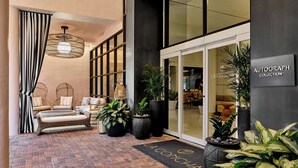 A modern hotel entrance with a black and white striped curtain, wicker furniture, potted plants, and a sign for the Autograph Collection. - La Concha Key West, Autograph Collection (Key West)