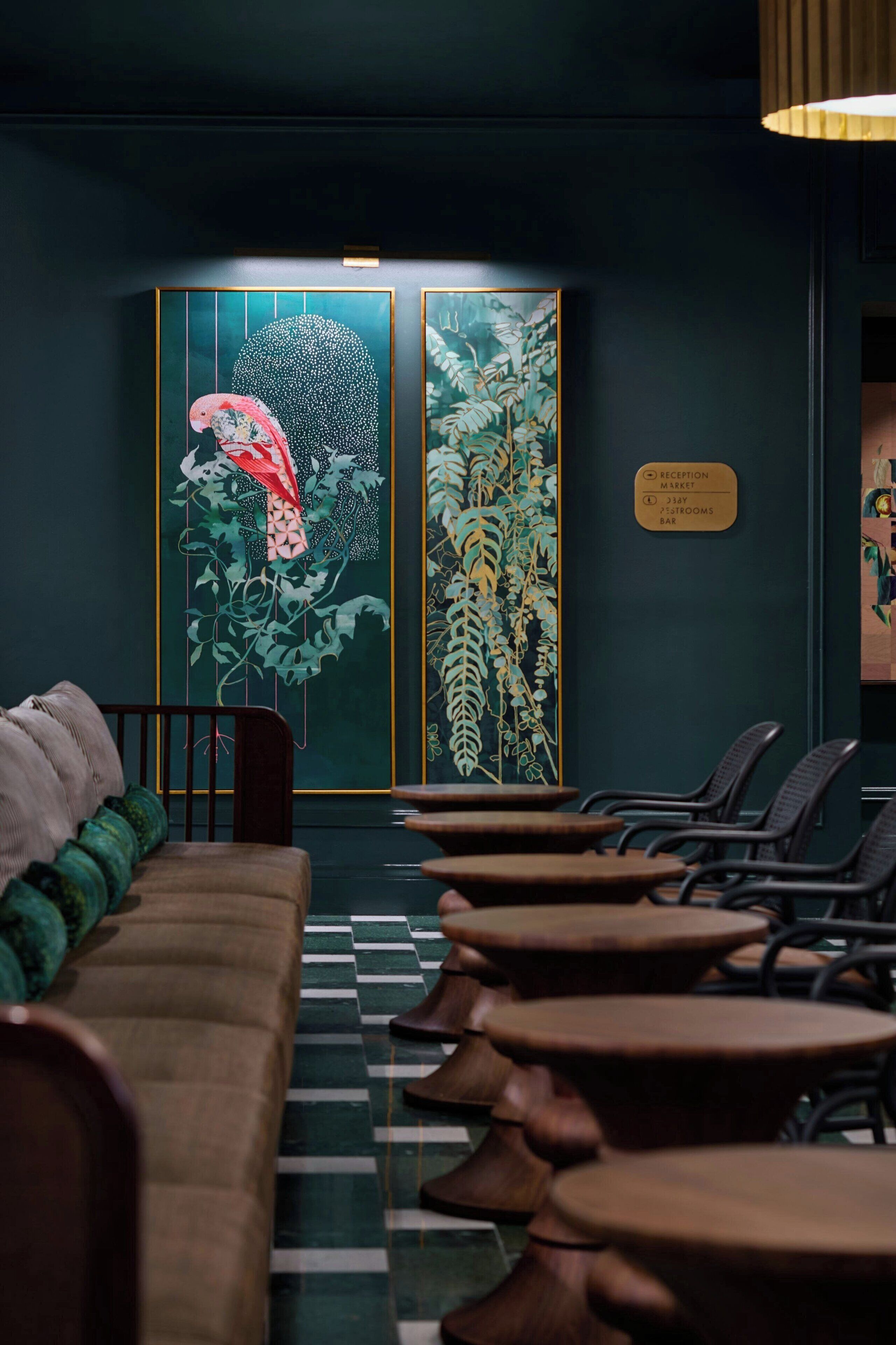 A reception area with a dark green wall, a reception desk, a sign indicating the location of the reception, market, and bar, and a row of chairs and tables.