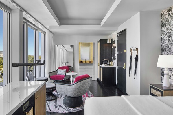 A modern hotel room with a large window, a desk, a chair, a bed, a vanity, and a bathroom.