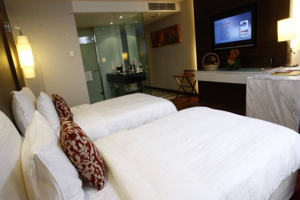 Hotelkamer met twee bedden, een bureau, een televisie en een zichtbare badkamer door een glazen deur.