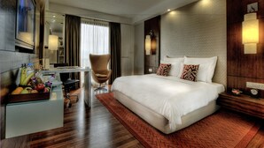 Hotelkamer met een groot bed, een bureau met stoel, een fruitmand en uitzicht op de stad.