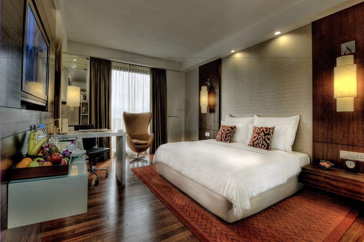 Hotelkamer met een groot bed, een bureau met stoel, een fruitmand en uitzicht op de stad.