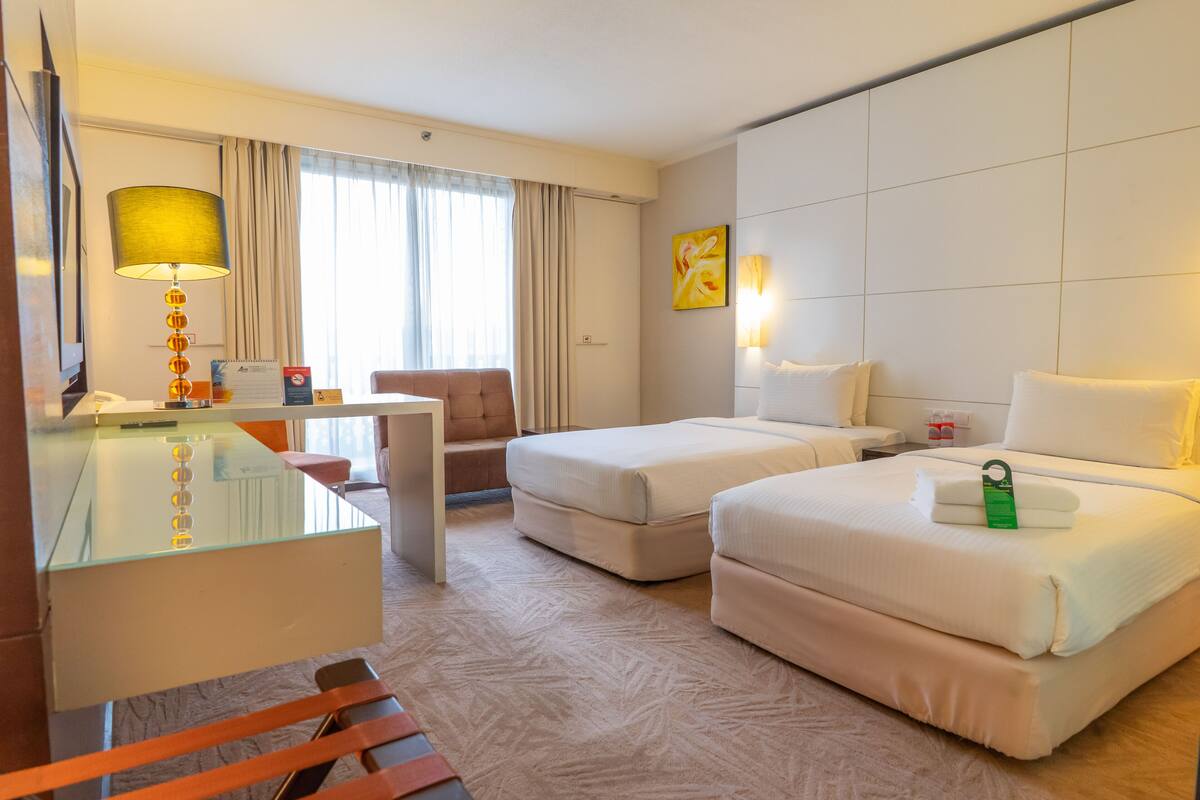 Een hotelkamer met twee bedden, een bureau, een stoel en een glazen tafel.