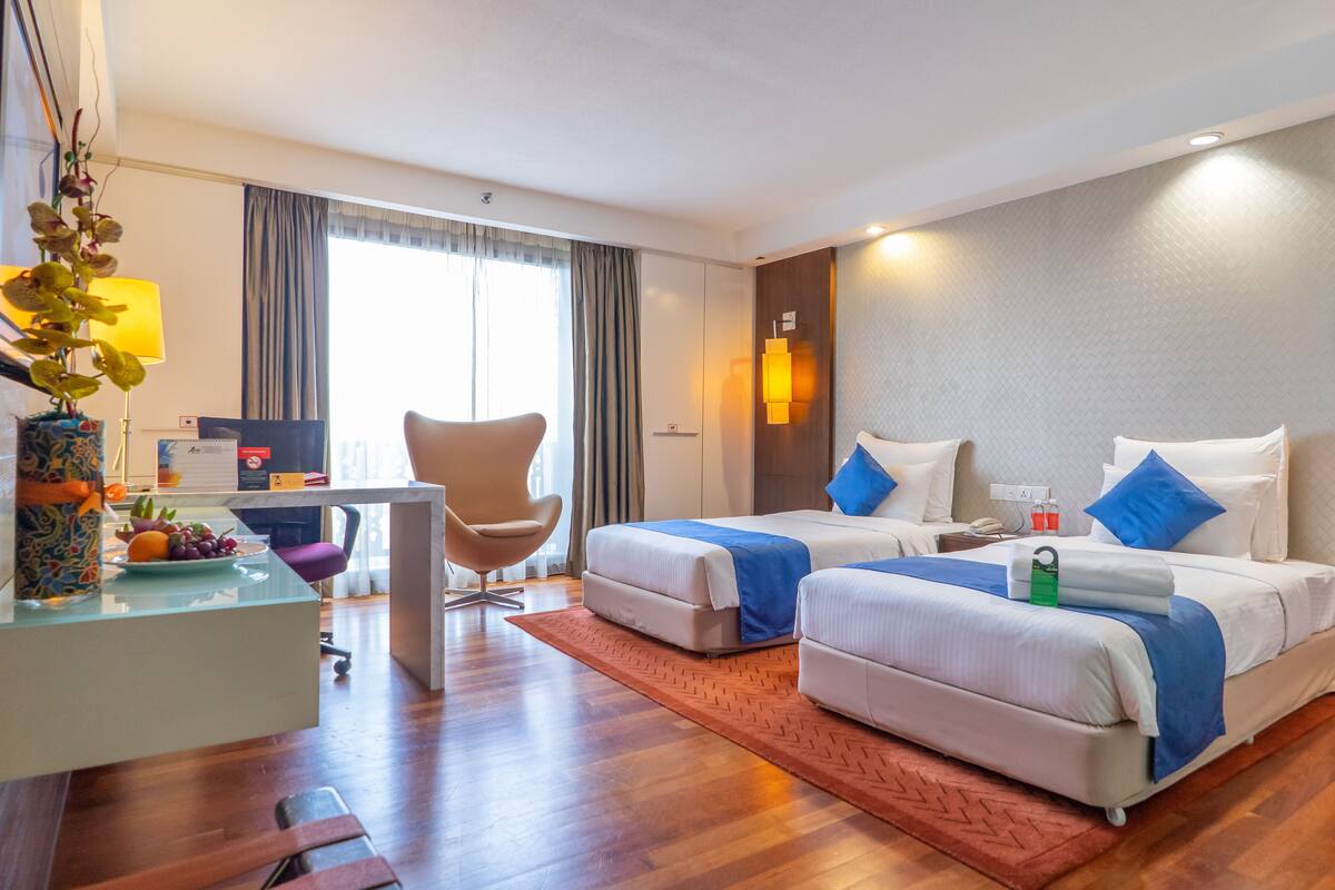 Een hotelkamer met twee bedden, een bureau, een stoel en een groot raam met gordijnen.