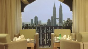 Een balkon met uitzicht op de Petronas Towers, ingericht met beige banken en een kleine tafel met een fles en servetten.
