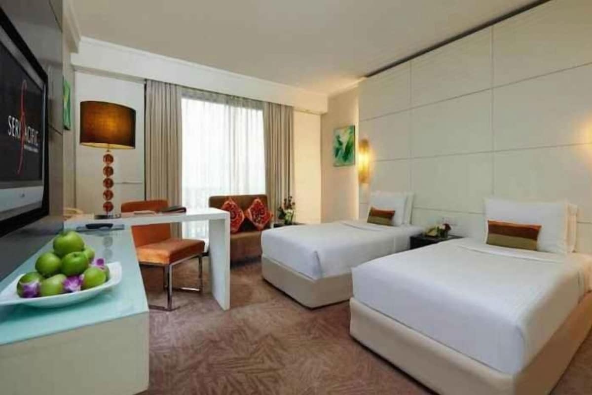 Een hotelkamer met twee bedden, een bureau, een televisie en een eettafel met fruit.
