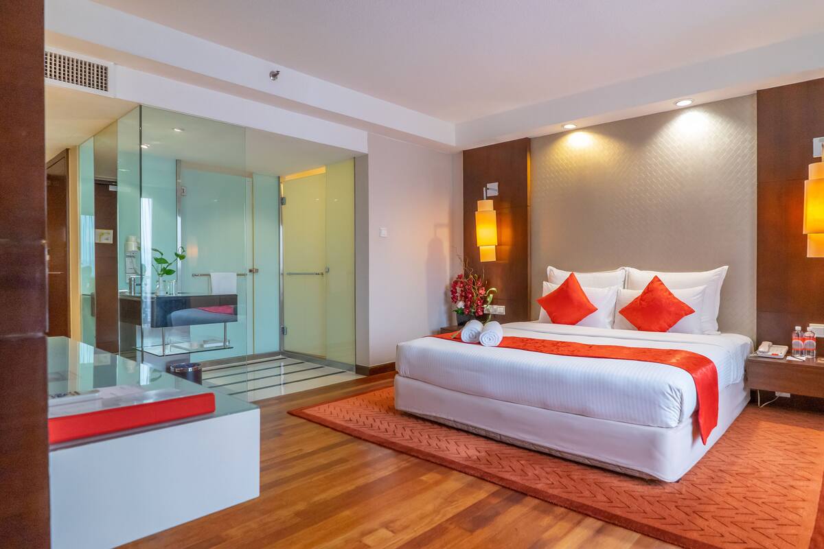 Een moderne hotelkamer met een groot bed, een douchecabine met glazen wanden en een houten vloer.