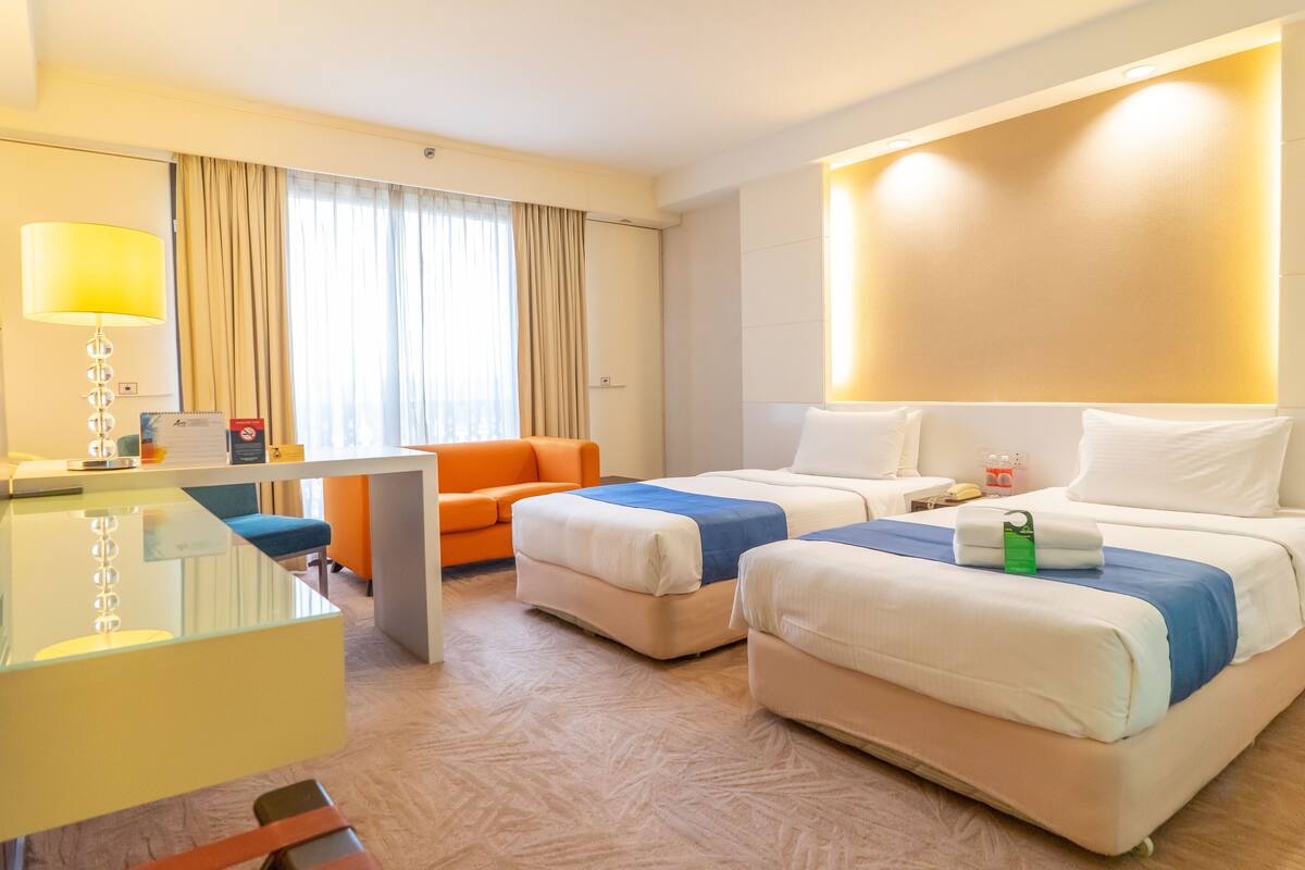 Een hotelkamer met twee bedden, een bureau, een stoel en een groot raam met gordijnen.