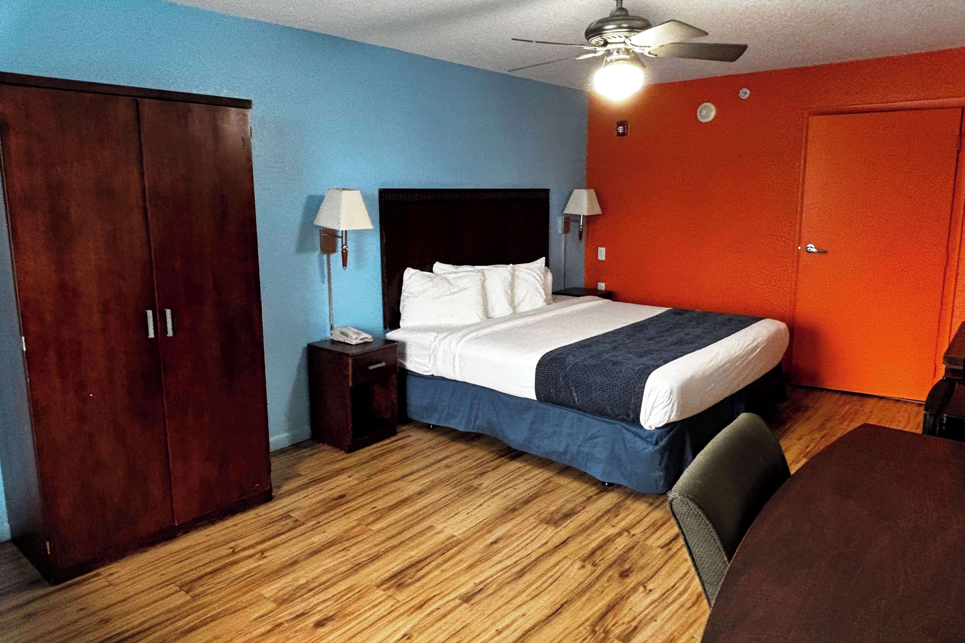 A hotel room with a bed, a desk, a chair, a wardrobe, and a ceiling fan.