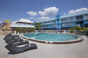 A swimming pool with lounge chairs, a building with blue and white exterior, and a clear sky. - Ramada by Wyndham Hotel & Water Park (Kissimmee)