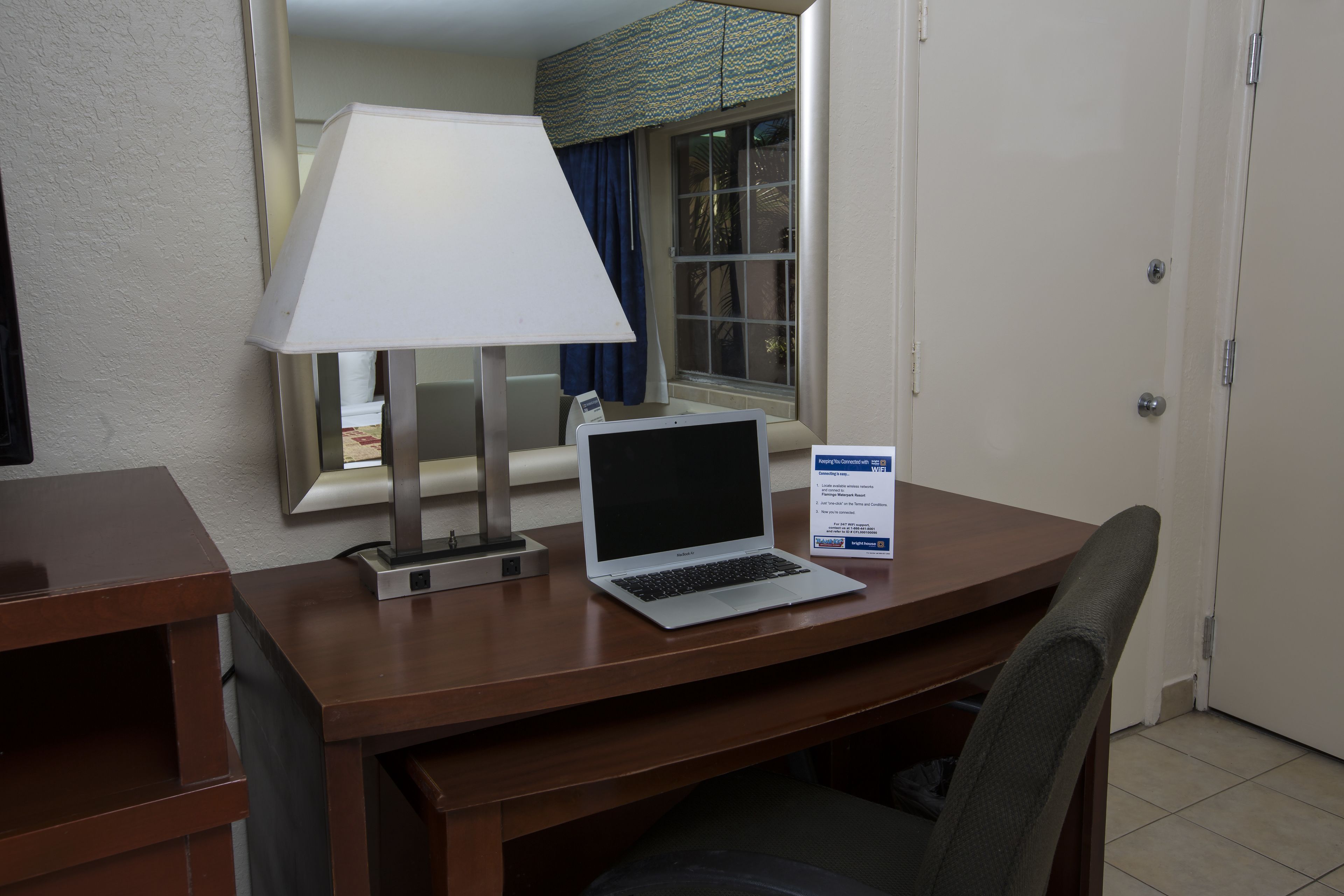 Et hotelværelse med skrivebord i træ, en bærbar computer, en lampe og et skilt med faciliteter.