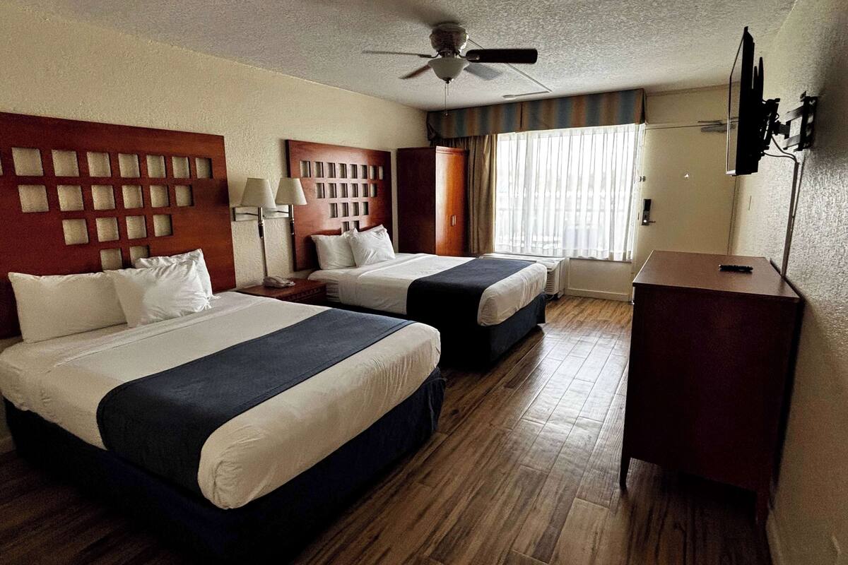 Een hotelkamer met twee bedden, een plafondventilator, een televisie en een houten vloer.