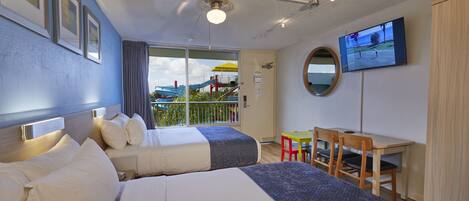 A hotel room with two beds, a desk, a chair, a TV, and a balcony with a view.