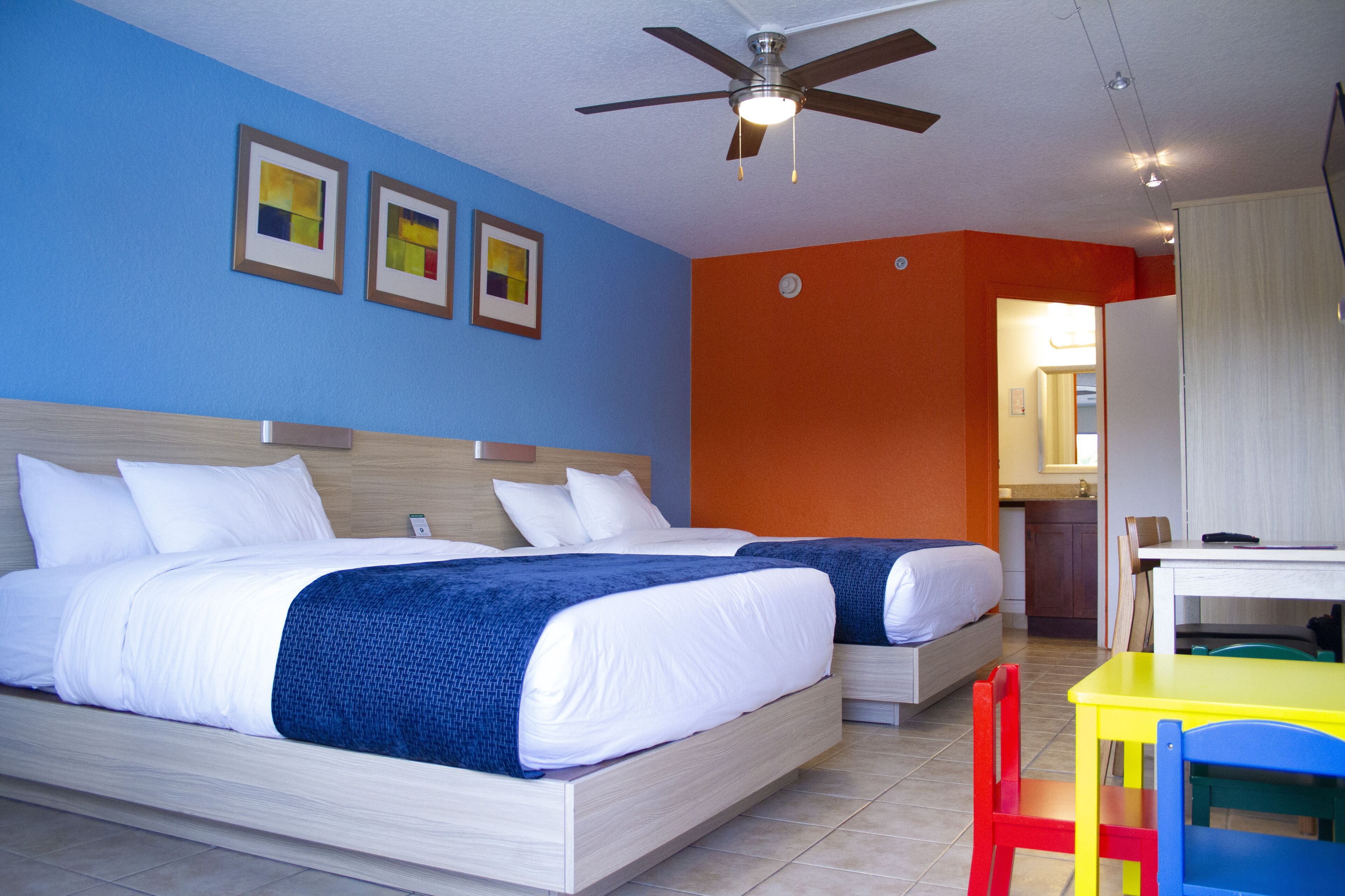 A hotel room with two beds, a ceiling fan, a small table, and a chair.