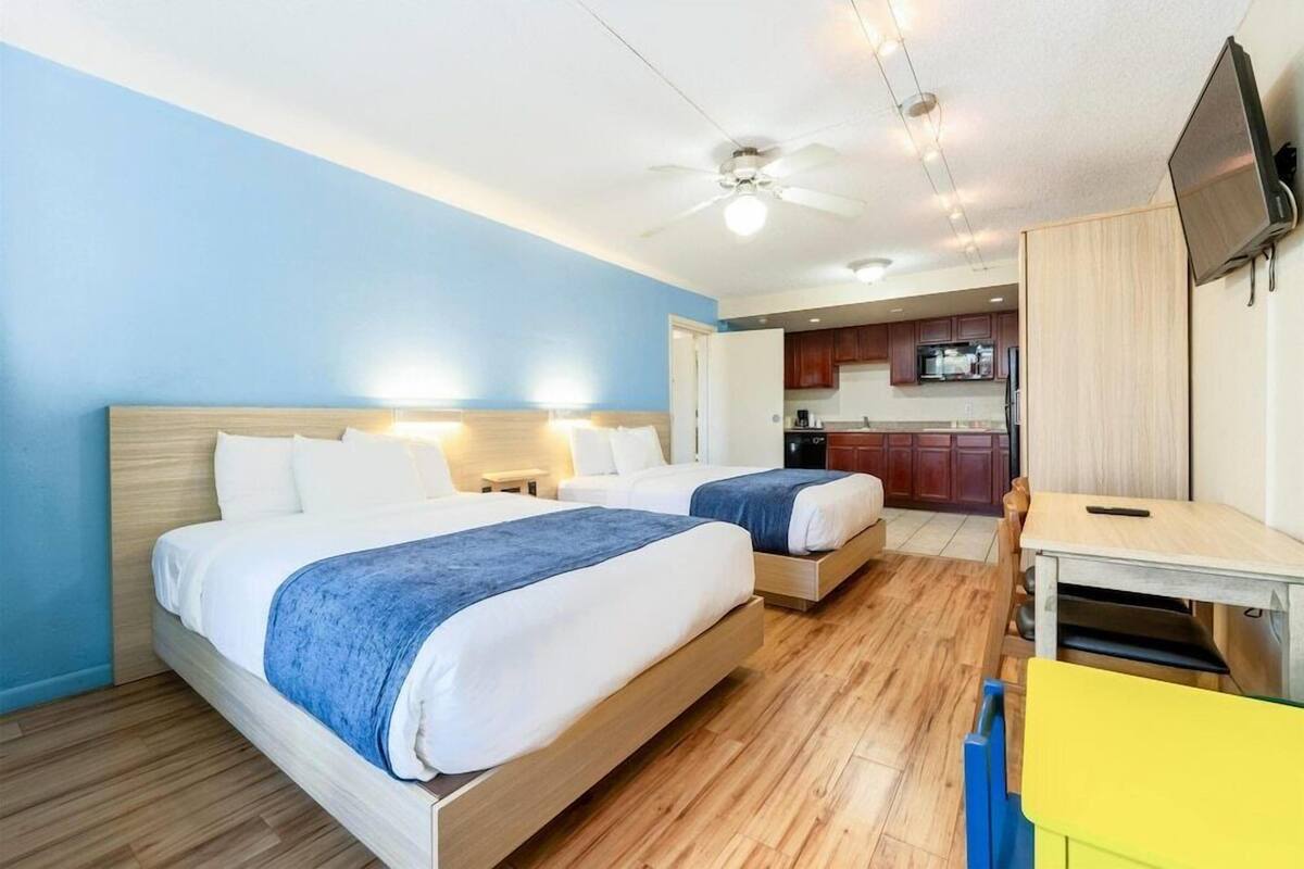 Een hotelkamer met twee bedden, een bureau, een stoel, een televisie en een kitchenette.