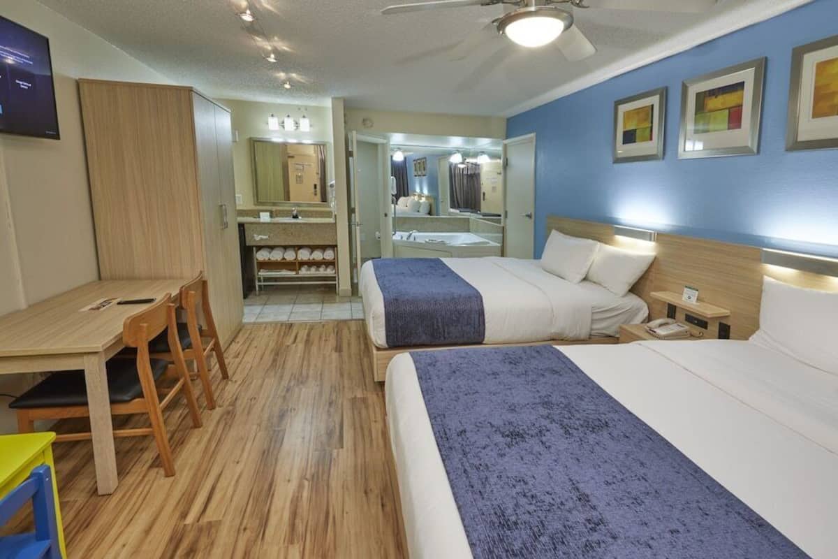 A hotel room with a bed, bedside table, desk, chairs, and a mirror.