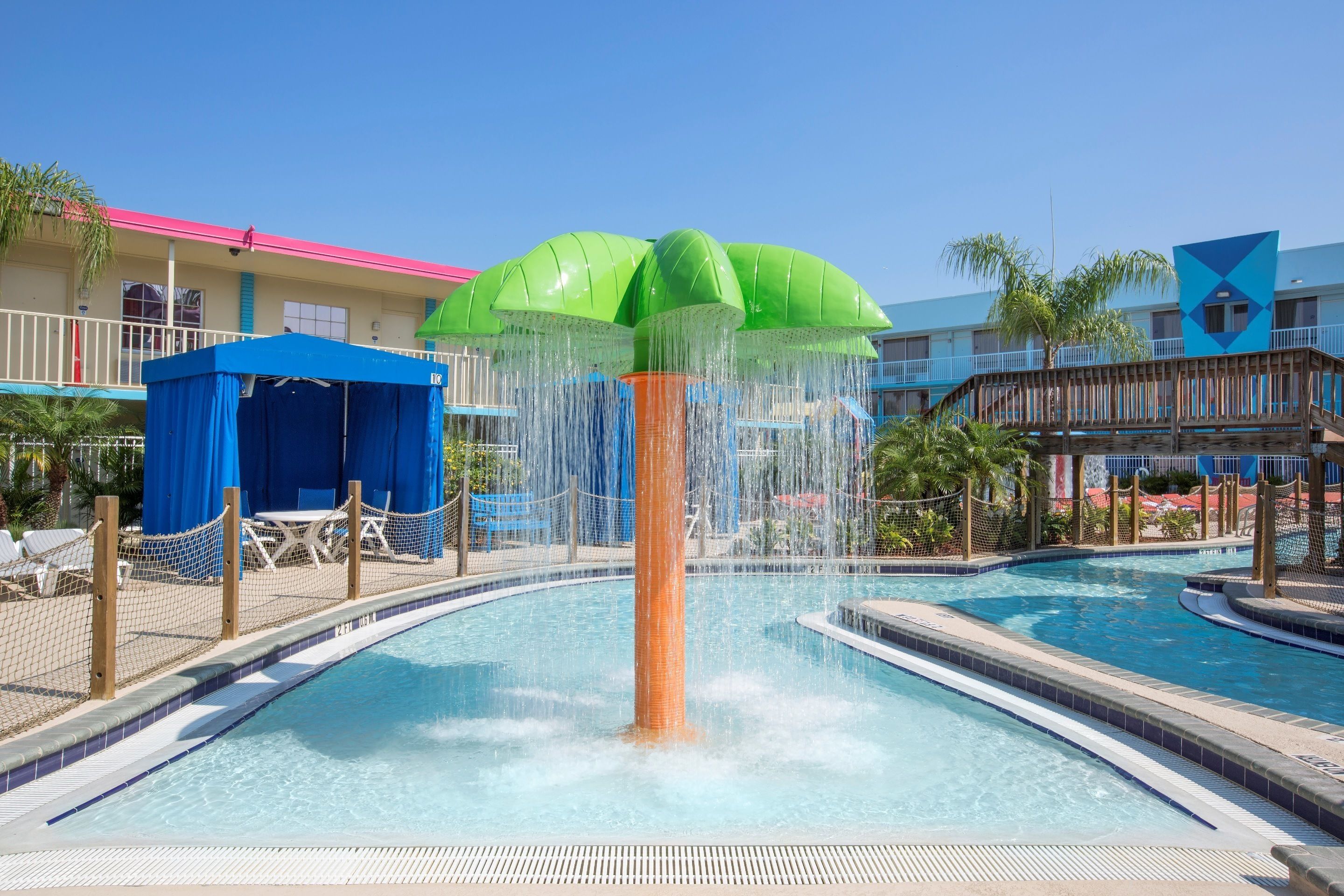 A pool area with a central water feature, a covered seating area, and a building with a pink roof.