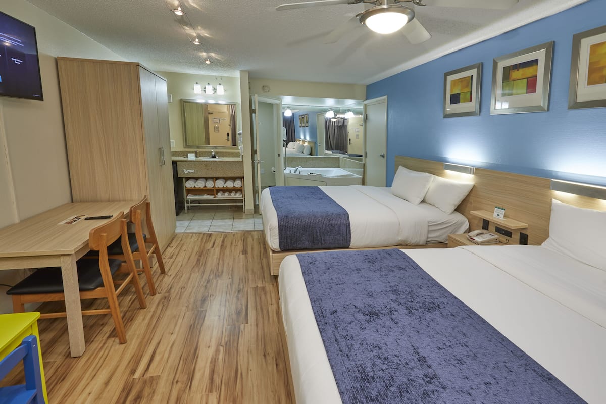 Een hotelkamer met twee bedden, een bureau, een stoel, een kledingkast en een badkamer zichtbaar door een open deur.