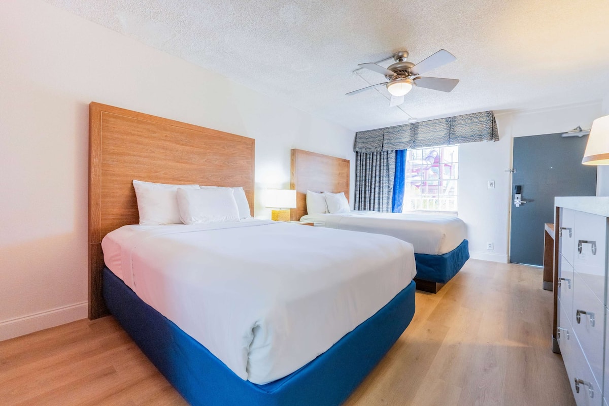 Een hotelkamer met twee bedden, een plafondventilator en een deur aan de rechterkant.