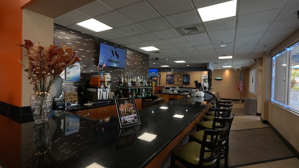 A bar area with a black countertop, seating, a large American flag, and a sign for a karaoke event. - Ramada by Wyndham Hotel & Water Park (Kissimmee)