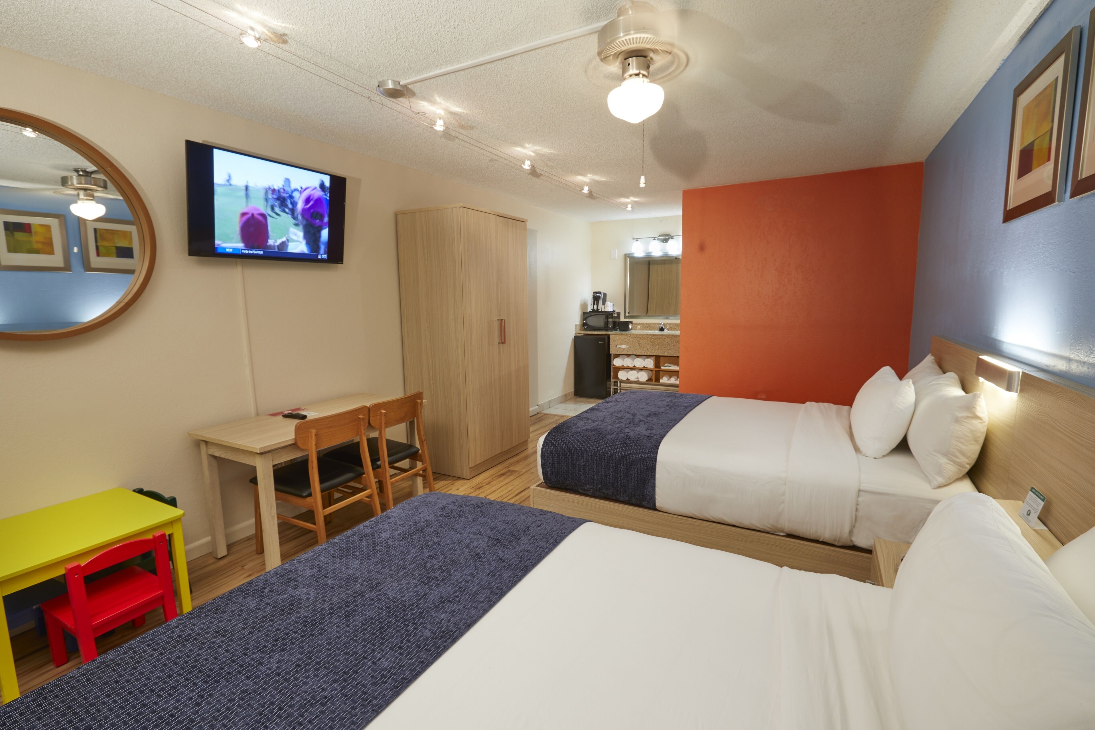 Una habitación de hotel con dos camas, un escritorio, una silla, un televisor y un espejo.